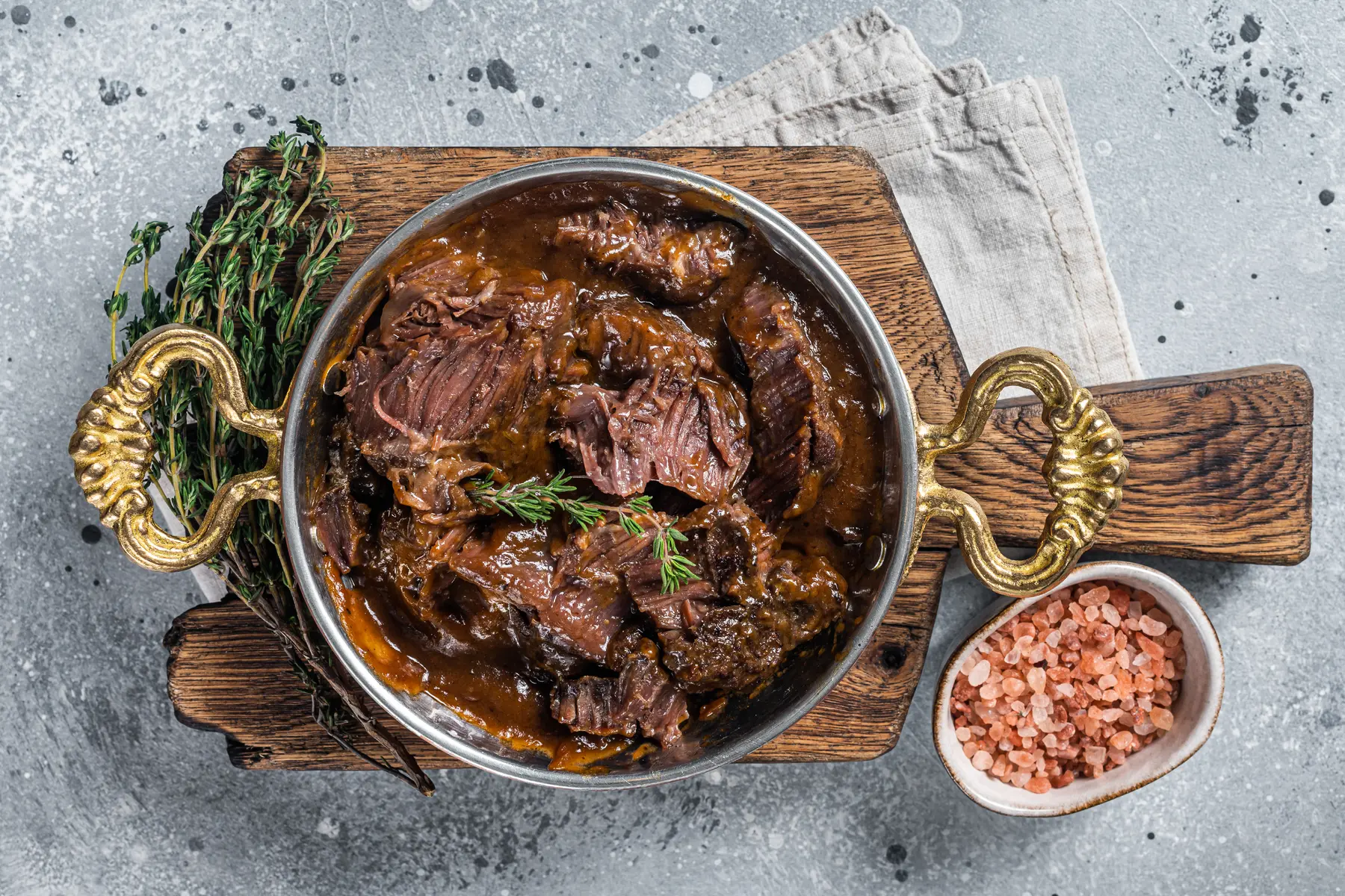 Geschmorte Rinderbäckchen in dunkler Sauce in einer Servierpfanne mit Kräutern