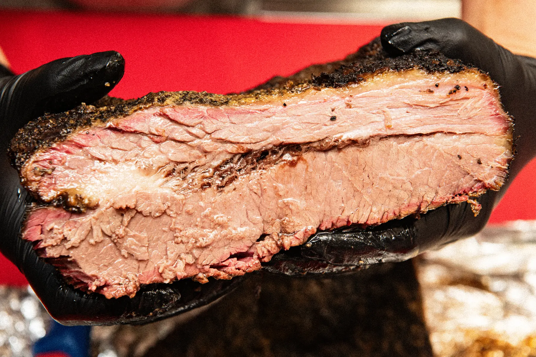 Anschnitt eines gegarten Briskets mit dunkler Kruste und glänzender Fettschicht, gehalten mit schwarzen Handschuhen
