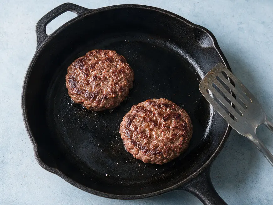 Zwei gebräunte Burger-Patties mit Abstand in einer flachen Pfanne