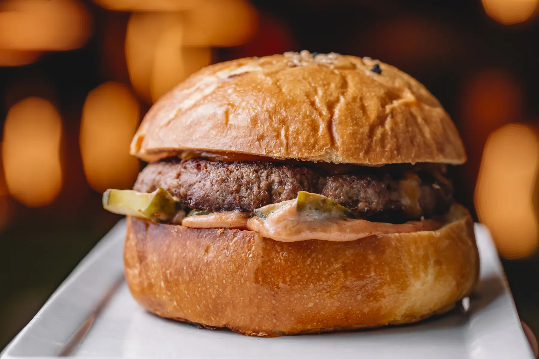 Burger mit einem Rindfleisch-Patty, Gurkenscheiben und Sauce im Brioche-Brötchen