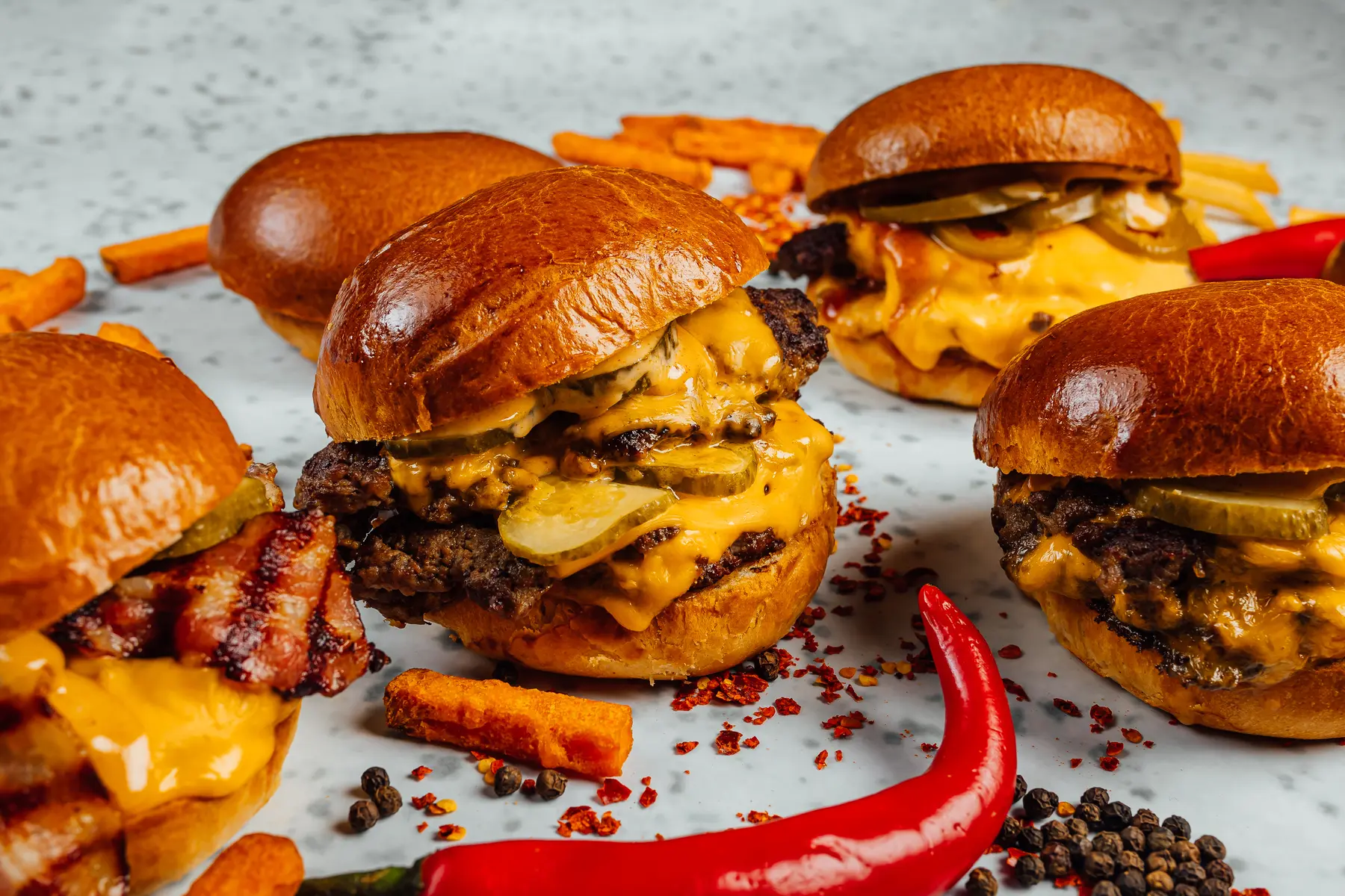 Mehrere gebaute Burger mit geschmolzenem Käse, Gewürzgurken und Pommes