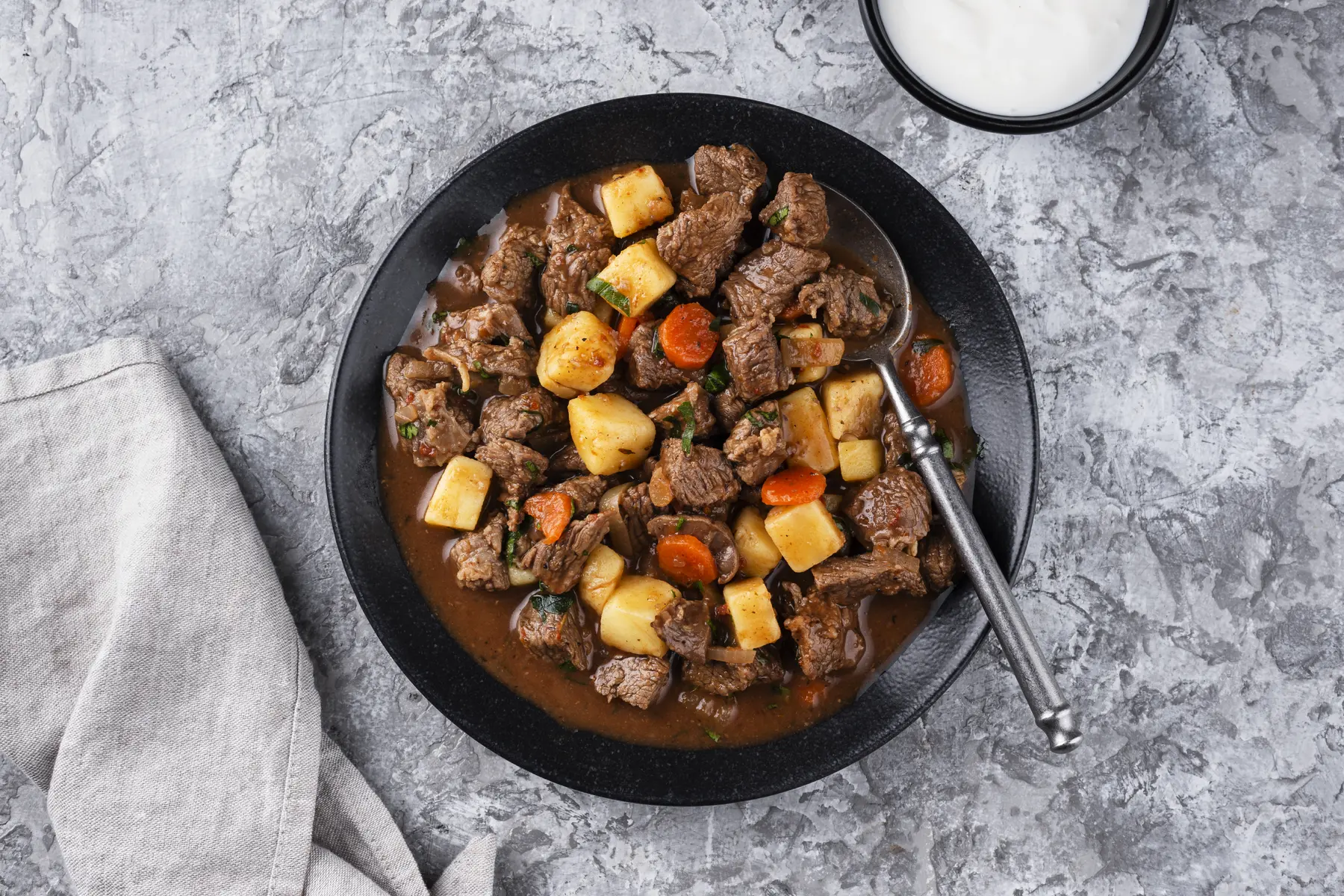 Rindergulasch mit Kartoffelwürfeln und Möhrenscheiben in einer dunklen Schale